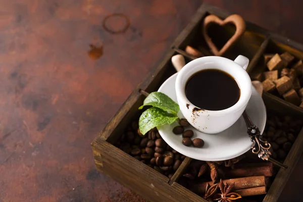 Kopp kaffe med cooffee bönor på en trälåda med korn av kaffe och kryddor på en sten bakgrund — Stockfoto