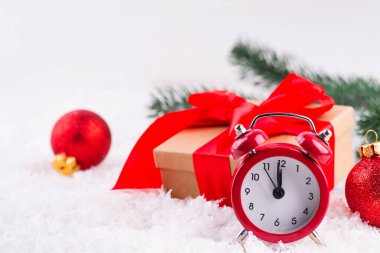 Kırmızı topları olan eski kırmızı bir saat, arka planda taze karın üzerinde duran büyük kırmızı bir fiyonklu kahverengi bir hediye kutusu. Noel zamanı