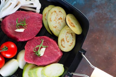 Köhne beton arka planda kızartılmaya hazır tavada çiğ biftek. Bitki, sarımsak, biber, tuz ve domatesli taze biftek..