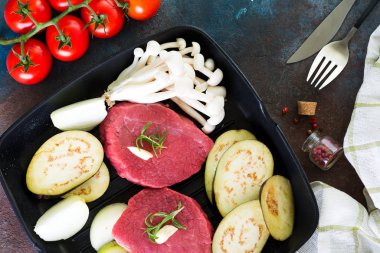 Köhne beton arka planda kızartılmaya hazır tavada çiğ biftek. Bitki, sarımsak, biber, tuz ve domatesli taze biftek..