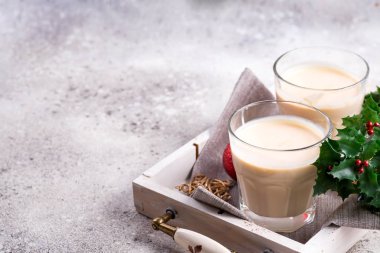 Baharatlı sıcak içecek, bardakta eggnog. Taş tabakta sinamon, hafif taş masada buz gibi dallar.