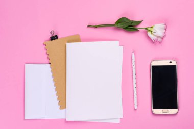 Çiçek kompozisyonu. Kağıt boşluğu, telefon ve pembe arka planda östoma pembe çiçekleri olan defter. Düz konum, üst görünüm, kare, kopyalama alanı