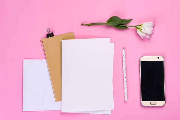 Bloemen samenstelling. Papier blanco, telefoon en notebook met eustoma roze bloemen op roze achtergrond. Flat lay, bovenaanzicht, vierkant, kopieerruimte — Stockfoto