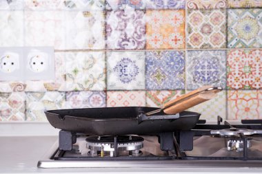 Eski renkli fayansların arka planındaki gaz sobasının üstünde boş ızgara tavası. Mutfak işleyici