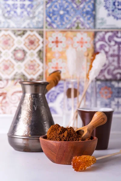 Caffè macinato in una ciotola di legno con bastoncino di zucchero di canna sullo sfondo di un turco di rame — Foto Stock