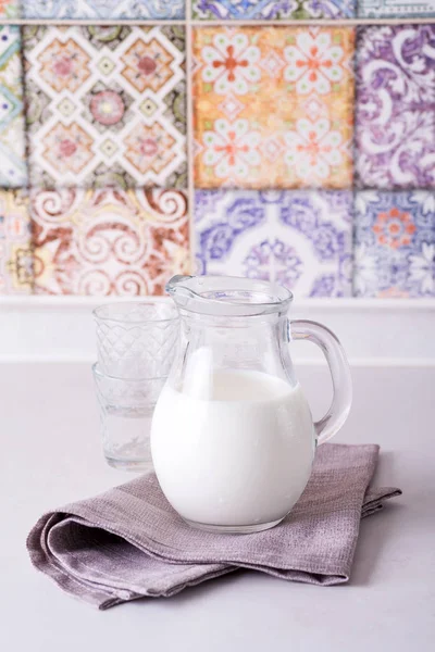 Frischmilch in Glaskanne und Glas auf Steintisch auf dem Hintergrund der alten farbigen Küchenfliesen — Stockfoto