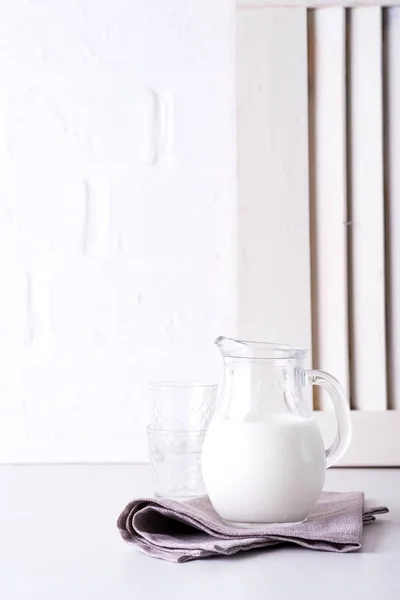Frischmilch in Glaskanne und Glas auf Steintisch vor dem Hintergrund der alten weißen Wand — Stockfoto