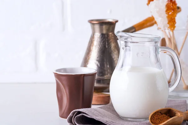 Krug mit Milch und gemahlenem Kaffee zum Zubereiten eines Drinks zu Hause auf einer steinernen Arbeitsplatte vor einer weißen Küchenwand — Stockfoto