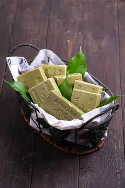 Bars of green natural olive oil soaps with green leaves in a basket on dark wooden background, top view — Stock Photo, Image