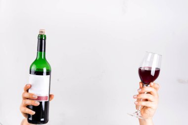 A woman hands holds glass with red wine and wine bottle on gray background with copy space