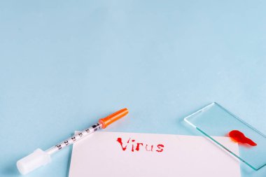 Şırıngalar ve üzerinde kan olan test tüpleri mavi arka planda beyaz kağıt ve yazıt virüsü ile