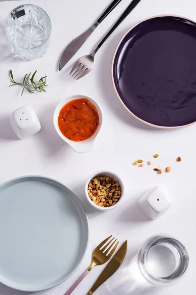 Leere runde blaue und lila Teller mit Besteck, gerösteten Erdnüssen und Tomatensauce auf weißem Hintergrund. Ansicht von oben mit Kopierraum für Ihr Design. — Stockfoto