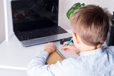 Okullu çocuk evdeki masada dizüstü bilgisayar kullanıyor, okul çocuğu ödevlerini yapıyor.