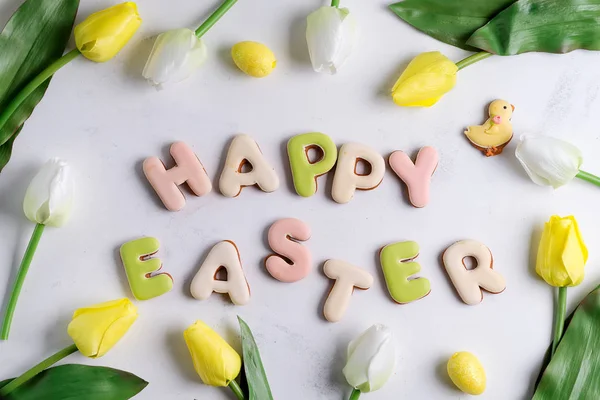 Tarjeta de felicitación de Pascua con patrón de flores de tulipán, huevos de Pascua y galleta de conejo. Vista superior sobre mesa de mármol blanco — Foto de Stock