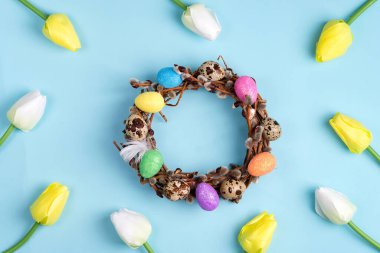 Paskalya söğüdü çelengi ve renkli Paskalya yumurtaları mavi arka planda lale çerçevesi. Üst görünüm, alanı kopyala