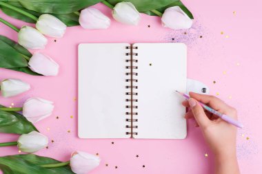 Pastel laleler, defter ve elle tutulan pembe arkaplanlı, yıldızlı bir kalem, kopyalama alanı