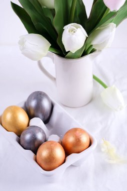 Seramik yumurta tepsisinde altın Paskalya Yumurtaları ve beyaz masa üzerinde lale. Paskalya arkaplanı veya paskalya kavramı.