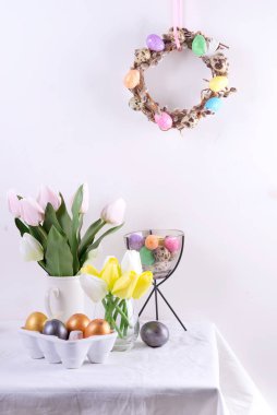 Paskalya sofrasında laleler, paskalya yumurtaları, kurabiyeler ve beyaz masada çelenkler.
