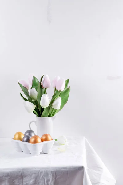 Ovos de Páscoa dourados em bandeja de ovos de cerâmica com tulipa na mesa branca. Contexto de Páscoa ou conceito de Páscoa . — Fotografia de Stock