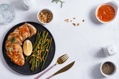 Kızarmış tavuk göğsü fileto, kuşkonmaz, sos ve limon tabakta ve beyaz taş arka planda