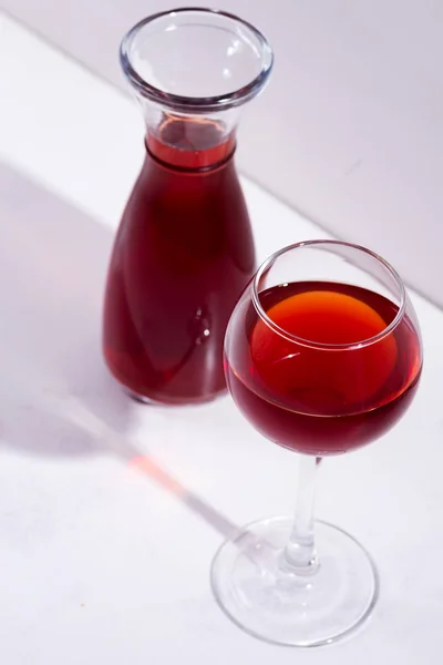 Красное вино в бокале и графин с тенями изолированы на белом камне фоне — стоковое фото