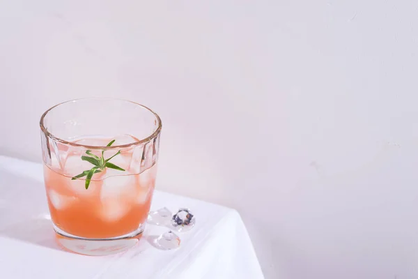 Cóctel rosa con romero y hielo en vaso sobre un mantel blanco sobre la mesa —  Fotos de Stock