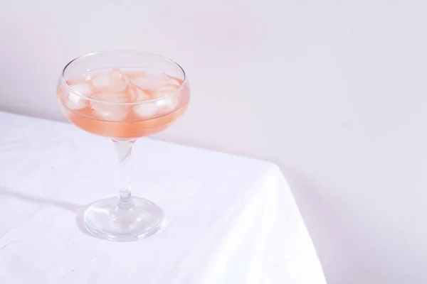 टेबलवर पांढरा टेबलक्लॉथवर रोझमरी आणि काचमध्ये बर्फसह गुलाबी कॉकटेल — स्टॉक फोटो, इमेज