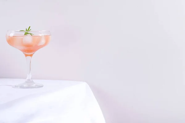 Cóctel rosa con romero y hielo en vaso sobre un mantel blanco sobre la mesa —  Fotos de Stock