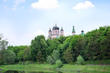City park area with green old trees, lake and beautiful view on the domes of Cathedral on a blue sky background.