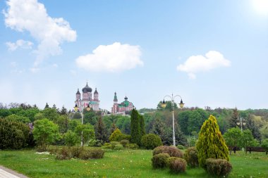 Public park landscape with view of big Church and decorative trees composition on a blue sky background.