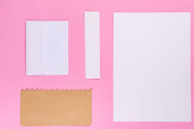 Blank craft envelope mock-up and blank pieces of paper on a pastel pink background. Flat lay