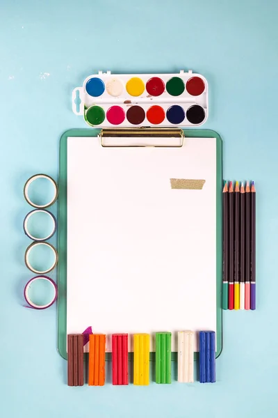 Espacio de trabajo del artista con colorido material de pintura y hojas de papel sobre un fondo azul pastel. Puesta plana — Foto de Stock