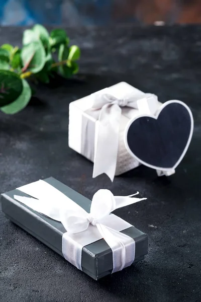 Gift boxes and chalkboard in the shape of heart with green plant twig on a dark stone background. — Stock fotografie