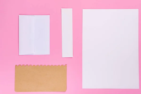 Mock-up de envelope de artesanato em branco e pedaços de papel em branco em um fundo rosa pastel. Depósito plano — Fotografia de Stock