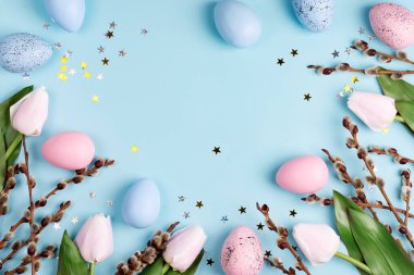 Taze lale çiçeklerinden, söğüt dallarından ve pastel mavi arka planda el yapımı renkli yumurtalardan oluşan bir tebrik kartı. Üst Manzara. Mesaj için yer. Mutlu Paskalyalar.