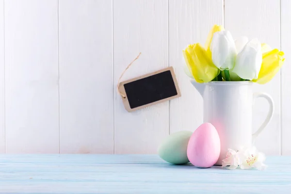 Congrats card from handmade painted multicolored eggs, tulips flowers and rectangular chalkboard for note or message against light grey wooden background, copy space. Happy Easter concept.