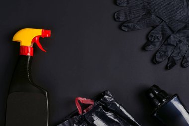 Siyah arka planda plastik sprey şişeler, çöp torbaları ve lastik eldivenler..