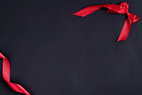 빨간색 리본 과 장식용 활로 된 모퉁이 프레임 이 있는 축제용 검은색 배경. — 스톡 사진