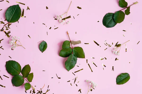 Cenário decorativo de decoração de confete brilhante, flores de Gypsophila e folhas verdes em um fundo rosa . — Fotografia de Stock