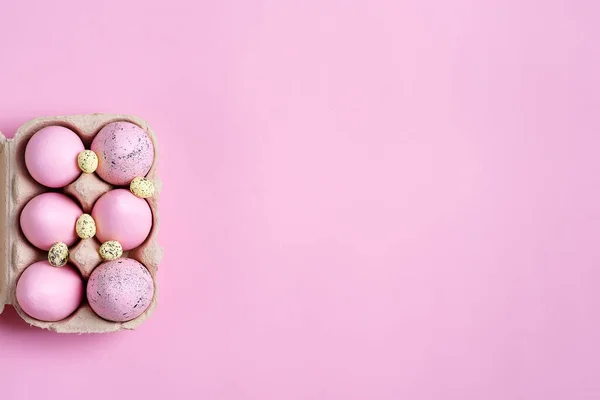 Marco festivo de Pascua de la caja de papel de huevos pintados rosados hechos a mano sobre un fondo del mismo color . —  Fotos de Stock