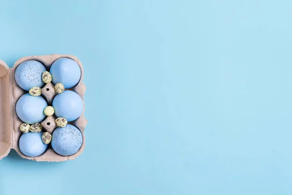 Marco festivo de Pascua de la caja de papel de huevos pintados azules hechos a mano sobre un fondo de color azul . —  Fotos de Stock