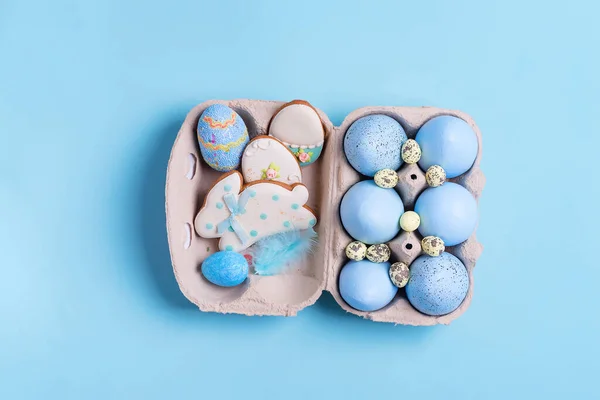 Composición de Pascua de huevos pintados artesanalmente en caja de papel y galletas horneadas sobre un fondo azul . —  Fotos de Stock