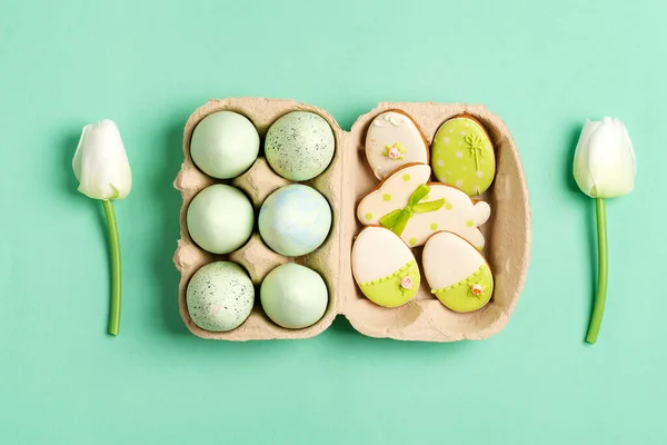 Composición de Pascua de huevos pintados artesanalmente en caja de papel, flores de tulipanes y galletas horneadas sobre un fondo verde . —  Fotos de Stock