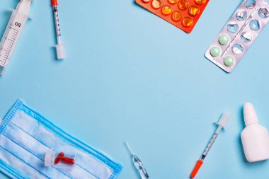 Açık mavi bir zemin üzerinde farklı tedaviler, tabletler, haplar ve plastik şırıngalarla tıbbi zemin.