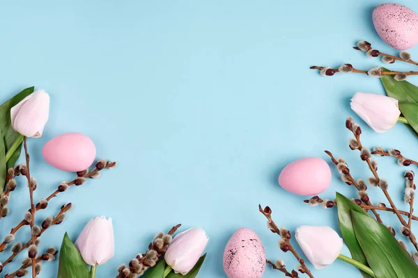 Marco con huevos pintados artesanalmente de Pascua, flores de tulipanes sobre un fondo azul claro . —  Fotos de Stock