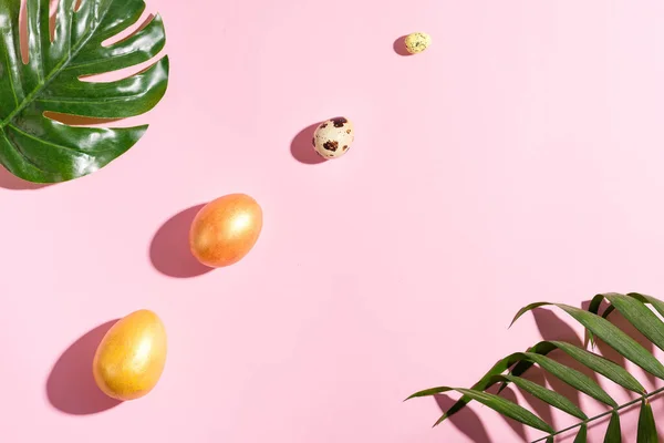 Tarjeta de vacaciones de Pascua con sombras de hojas de palma tropical, pollo pintado de oro y huevos de codorniz sobre un fondo rosa pastel . —  Fotos de Stock