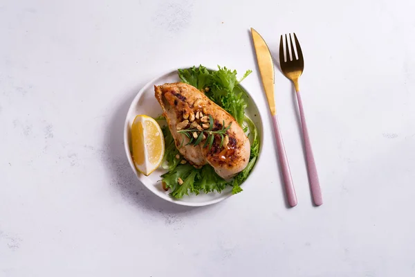 Grilled chicken breast fillet with asparagus and lemon in slate plate and white stone background — Stock Photo, Image