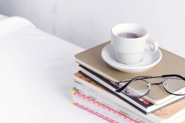 Üzerinde kadın bardakları ve beyaz bir masanın üstünde kahve fincanı olan bir yığın kitap ve not defteri..