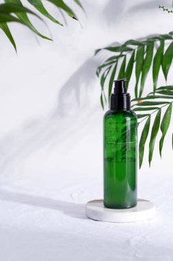 Beyaz tekstil arka planında temiz cilt için doğal losyon içeren yeşil plastik şişe yeşil tropikal yapraklar..