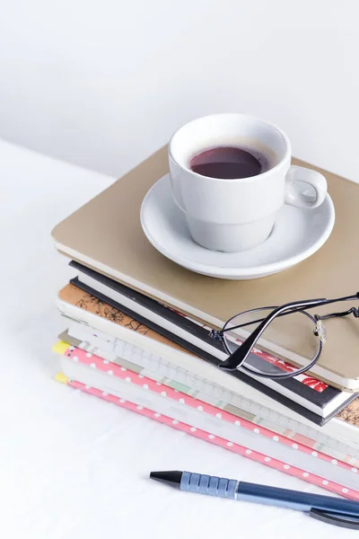 Pilha de diferentes livros e blocos de notas com copos femininos e xícara de café no topo em uma mesa branca . — Fotografia de Stock